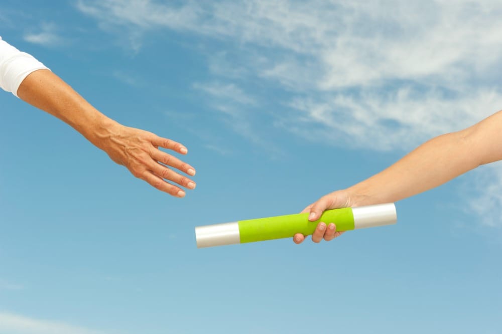 Why Does the Journey Matter More Than the Destination? Hands of track and field athletes with relay baton, symbol for teamwork, partnership, cooperation, isolated with blue sky as background and copy space.